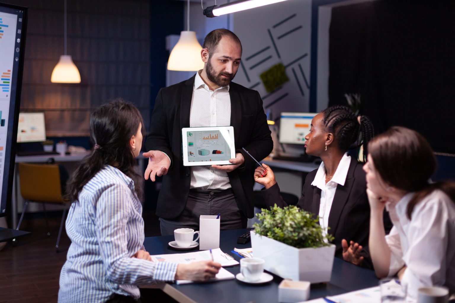 Team of professionals reviewing analytics as a colleague presents financial charts on a digital tablet.