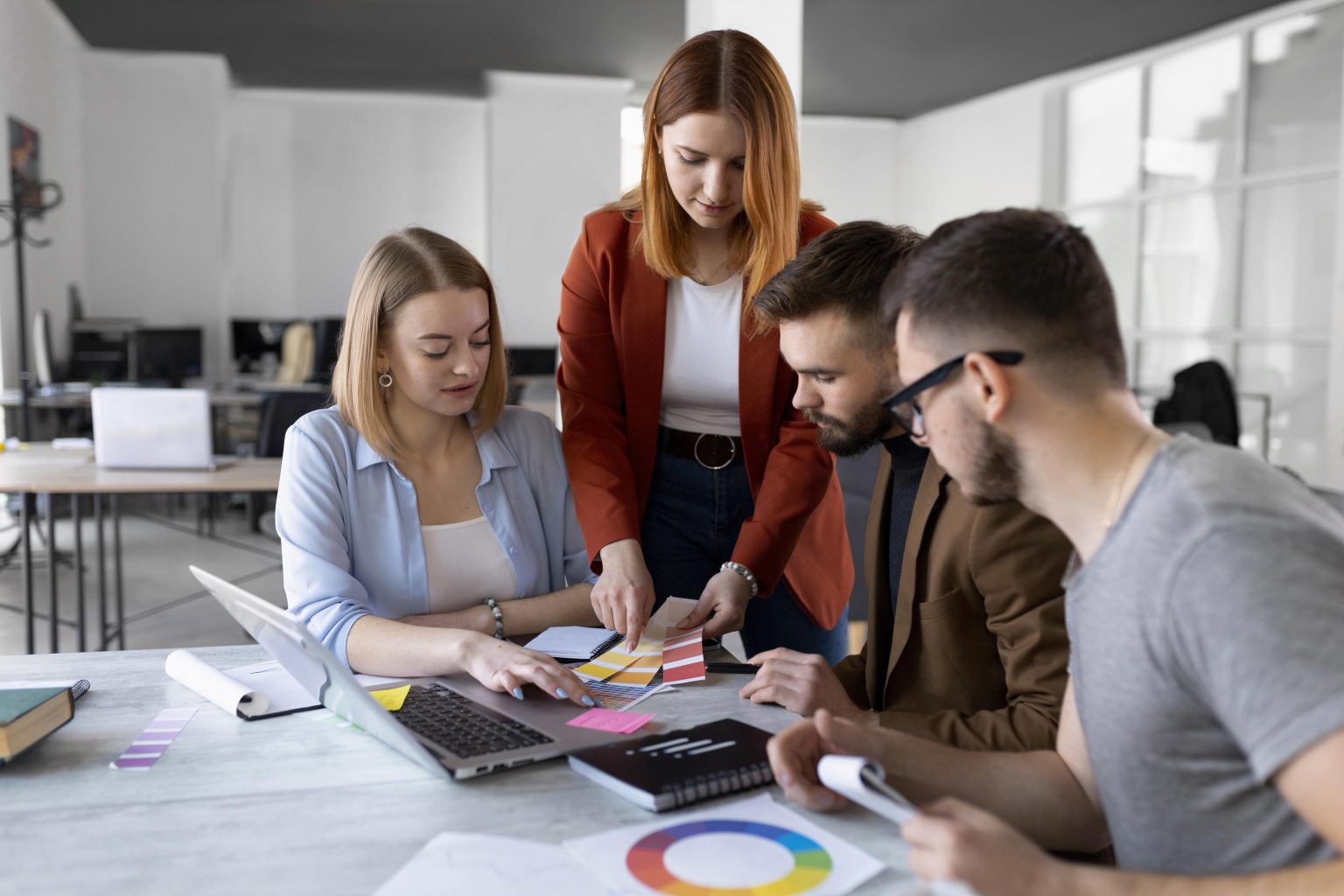 Creative team at a digital marketing agency in Dubai brainstorming brand identity concepts using color palettes, a laptop, and design tools in a modern office.