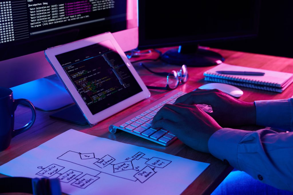 A programmer working at a desk with multiple screens displaying code and a tablet, representing a professional web development company Dubai.