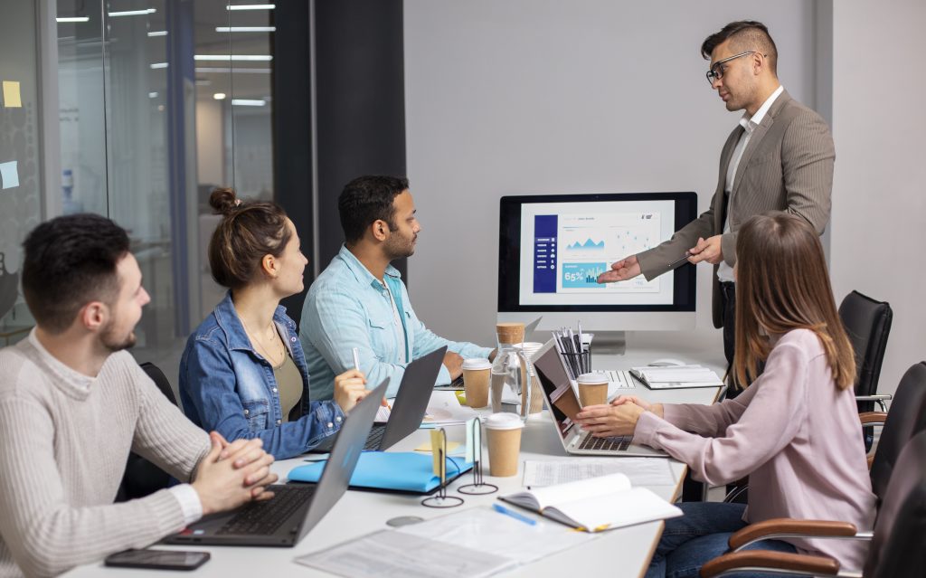 Business team attending a digital marketing presentation in a modern office meeting room with laptops, charts, and analytics displayed on a screen.