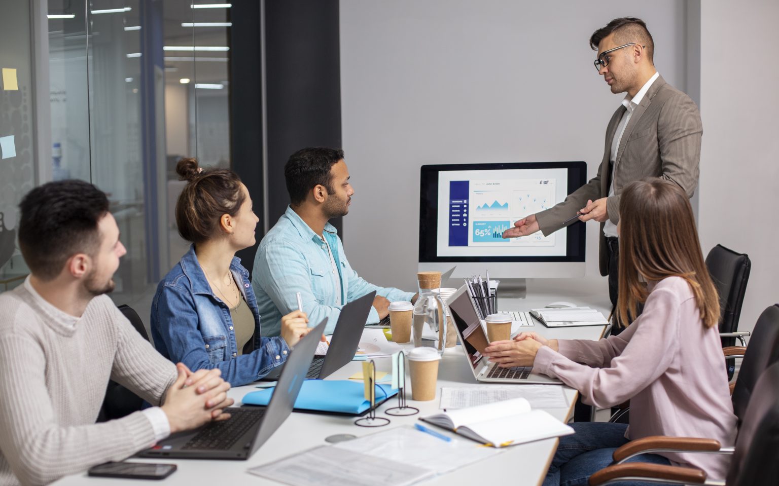 Business team attending a digital marketing presentation in a modern office meeting room with laptops, charts, and analytics displayed on a screen.