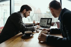 Two professionals collaborating over coffee while analyzing dashboard metrics and UI designs on a laptop screen.