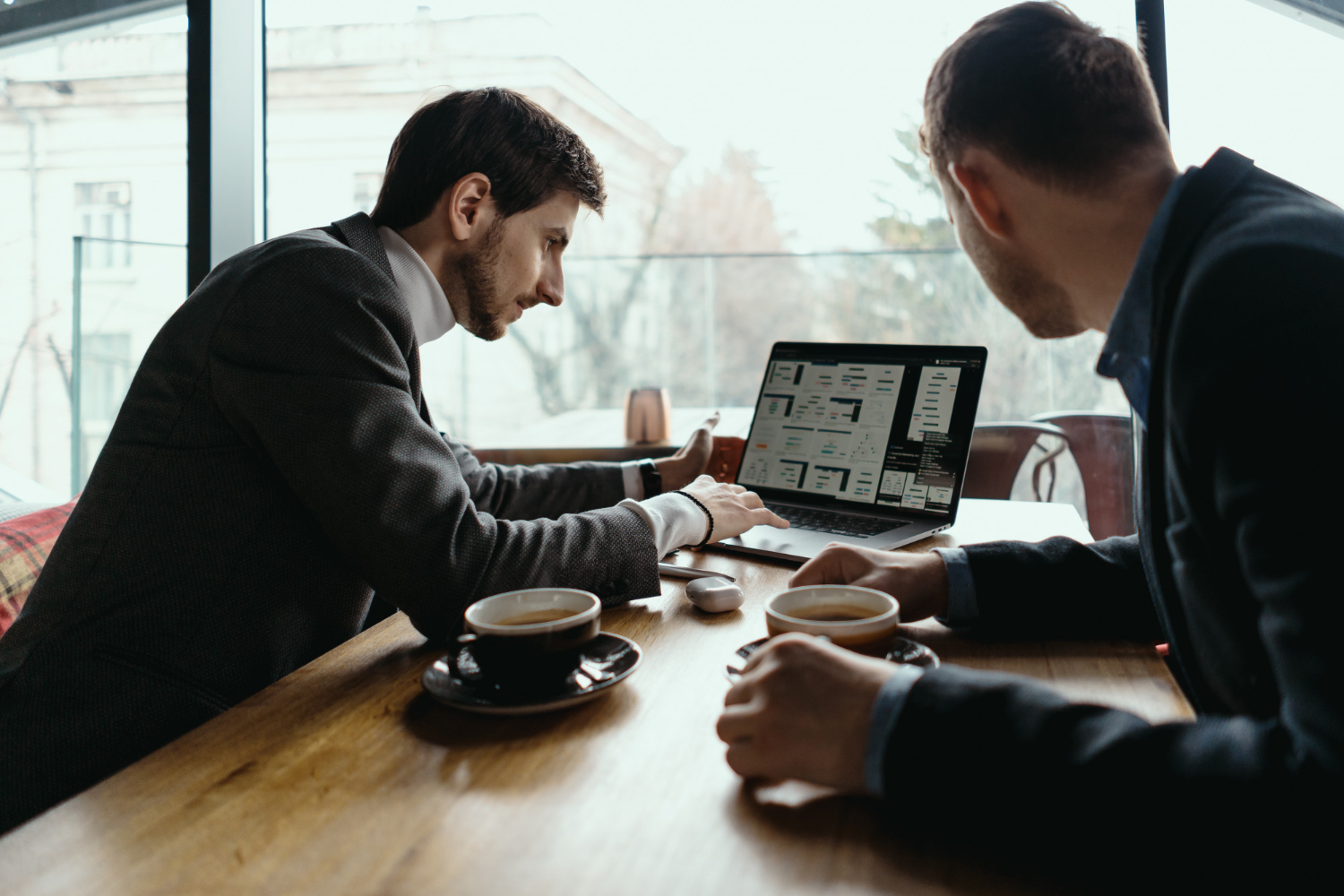Two professionals collaborating over coffee while analyzing dashboard metrics and UI designs on a laptop screen.