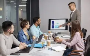 Business team attending a digital marketing presentation in a modern office meeting room with laptops, charts, and analytics displayed on a screen.